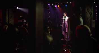 Movie still from “Annie Hall” (1977), directed by Woody Allen – A man standing in front of a microphone on a stage; Wide shot, Over the shoulder angle