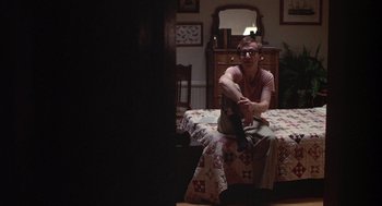Movie still from “Annie Hall” (1977), directed by Woody Allen – A man sitting on top of a bed next to a dresser; Wide shot, Low angle