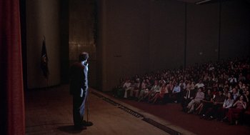 Movie still from “Annie Hall” (1977), directed by Woody Allen – A man standing on a stage in front of an audience; Wide shot, High angle