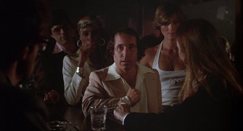 Movie still from “Annie Hall” (1977), directed by Woody Allen – A group of people sitting at a table with a glass of water; Medium shot, Over the shoulder angle