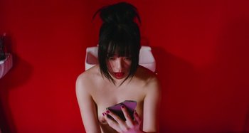 Movie still from “Antiporno” (2016), directed by Sion Sono – A woman sitting on a toilet looking at her cell phone; Close Up shot, Overhead angle
