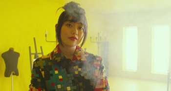 Movie still from “Antiporno” (2016), directed by Sion Sono – A woman with a colorful shirt and a bun in her hair; Close Up shot, Low angle