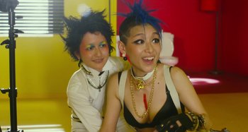 Movie still from “Antiporno” (2016), directed by Sion Sono – Two young women with punk hair and make - up posing for a picture; Medium shot, Low angle