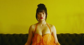 Movie still from “Antiporno” (2016), directed by Sion Sono – A woman sitting on top of a couch wearing a yellow dress; Medium shot, Low angle