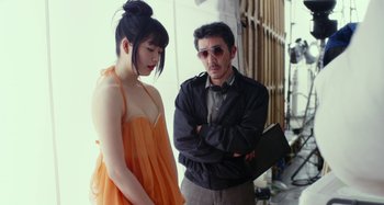 Movie still from “Antiporno” (2016), directed by Sion Sono – A man standing next to a woman in an orange dress; Medium shot, Over the shoulder angle