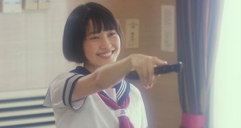 Movie still from “Antiporno” (2016), directed by Sion Sono – A young woman holding a remote control in her hand; Close Up shot, Over the shoulder angle