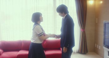 Movie still from “Antiporno” (2016), directed by Sion Sono – A man and a woman shaking hands in front of a red couch; Medium shot, Low angle