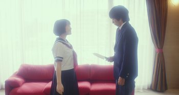 Movie still from “Antiporno” (2016), directed by Sion Sono – A man and a woman in school uniforms holding a knife in front of a red couch; Medium shot, Low angle