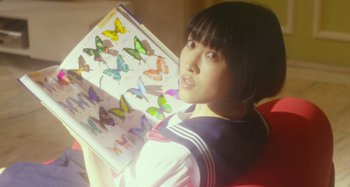 Movie still from “Antiporno” (2016), directed by Sion Sono – A woman is holding a book with butterflies on it; Close Up shot, High angle
