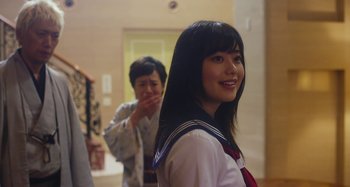 Movie still from “Antiporno” (2016), directed by Sion Sono – A young woman in a school uniform smiles for the camera; Medium shot, Over the shoulder angle