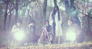 Movie still from “Antiporno” (2016), directed by Sion Sono – A group of people sitting in the grass with trees in the background; Wide shot, Low angle