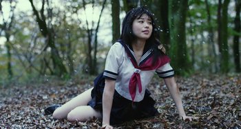Movie still from “Antiporno” (2016), directed by Sion Sono – A young girl sitting on the ground in the leaves; Medium shot, High angle