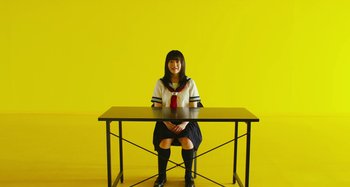 Movie still from “Antiporno” (2016), directed by Sion Sono – A woman sitting at a table in front of a yellow wall; Wide shot, High angle