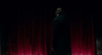 Movie still from “Antiviral” (2012), directed by Brandon Cronenberg – A person standing in front of a stage curtain; Wide shot, Low angle