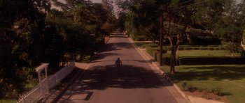 Movie still from “Apt Pupil” (1998), directed by Bryan Singer – A person riding a motorcycle down a street; Extreme Wide shot, High angle