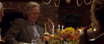 Movie still from “Apt Pupil” (1998), directed by Bryan Singer – An older man sitting at a dinner table holding a cigar; Medium shot, Over the shoulder angle