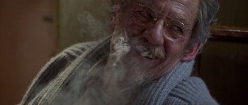 Movie still from “Apt Pupil” (1998), directed by Bryan Singer – An old man with a beard and glasses smoking a cigarette; Close Up shot, Over the shoulder angle