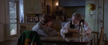Movie still from “Apt Pupil” (1998), directed by Bryan Singer – Two people sitting at a table in a kitchen; Medium shot, Over the shoulder angle
