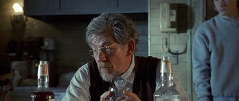 Movie still from “Apt Pupil” (1998), directed by Bryan Singer – An older man sitting at a table drinking a glass of water; Close Up shot, Over the shoulder angle