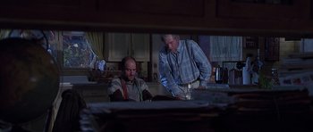 Movie still from “Apt Pupil” (1998), directed by Bryan Singer – Two men are standing in a kitchen at night; Medium shot, Over the shoulder angle