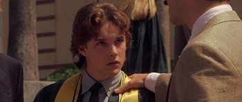 Movie still from “Apt Pupil” (1998), directed by Bryan Singer – A young man in a graduation gown is being hugged by a man in a suit; Close Up shot, Over the shoulder angle