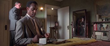 Movie still from “Apt Pupil” (1998), directed by Bryan Singer – A man in a suit and tie looking at a stack of papers; Medium shot, Over the shoulder angle