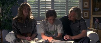 Movie still from “Apt Pupil” (1998), directed by Bryan Singer – Three people sitting on a couch looking at papers; Medium shot, Over the shoulder angle
