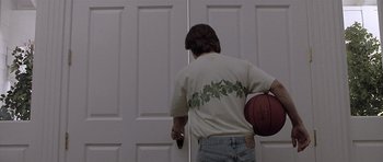 Movie still from “Apt Pupil” (1998), directed by Bryan Singer – A man holding a basketball in front of a door; Medium shot, Over the shoulder angle