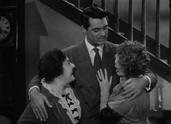 Movie still from “Arsenic and Old Lace” (1944), directed by Frank Capra – Two women and a man standing next to each other in front of a staircase; Medium shot, High angle