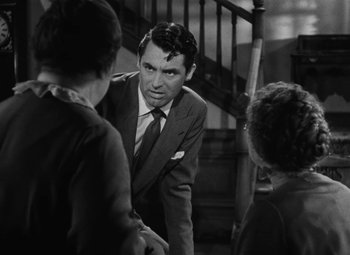 Movie still from “Arsenic and Old Lace” (1944), directed by Frank Capra – A man in a suit and tie standing next to two women; Medium shot, Over the shoulder angle