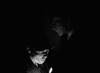 Movie still from “Arsenic and Old Lace” (1944), directed by Frank Capra – Two men in the dark looking at a cell phone; Medium shot, Over the shoulder angle