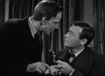 Two men in a room one is holding something in his hand and the other is holding something in his other hand