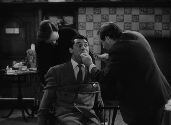 Movie still from “Arsenic and Old Lace” (1944), directed by Frank Capra – A black and white photo of a man getting his teeth waxed; Medium shot, Over the shoulder angle