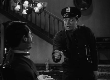 Movie still from “Arsenic and Old Lace” (1944), directed by Frank Capra – A cop talking to a man sitting at a dinner table; Medium shot, Over the shoulder angle