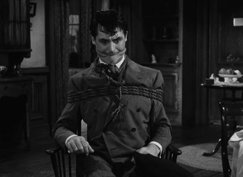 Movie still from “Arsenic and Old Lace” (1944), directed by Frank Capra – A black and white photo of a man in a suit and tie; Close Up shot, High angle