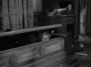 Movie still from “Arsenic and Old Lace” (1944), directed by Frank Capra – A cat is hiding in a wooden box in a room; Medium shot, High angle