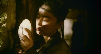 Movie still from “Ashes of Time” (1994), directed by Kar-Wai Wong – A person holding an object up to their face; Close Up shot, Low angle