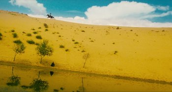 Movie still from “Ashes of Time” (1994), directed by Kar-Wai Wong – A man riding a horse down a dirt hill next to a lake; Extreme Wide shot, High angle