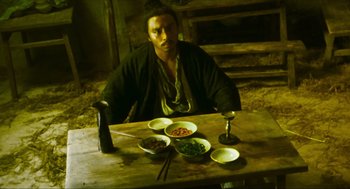 Movie still from “Ashes of Time” (1994), directed by Kar-Wai Wong – A man sitting at a wooden table with bowls of food; Medium shot, High angle