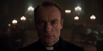 Movie still from “Dark” (2017), created by Baran bo Odar – A man wearing a priest's collar stares into the camera; Close Up shot, Low angle