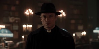 Movie still from “Dark” (2017), created by Baran bo Odar – A man wearing a priest's outfit and a hat; Close Up shot, Low angle