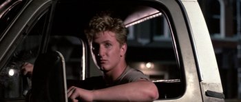 Movie still from “At Close Range” (1986), directed by James Foley – A man sitting in the driver's seat of a car; Close Up shot, Low angle