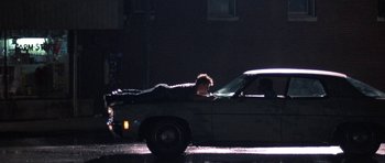 Movie still from “At Close Range” (1986), directed by James Foley – A man laying on the hood of a parked car; Wide shot, Overhead angle