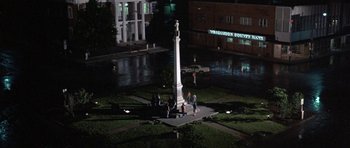 Movie still from “At Close Range” (1986), directed by James Foley – A group of people standing in front of a monument at night; Extreme Wide shot, High angle