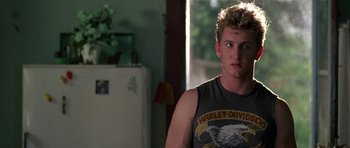 Movie still from “At Close Range” (1986), directed by James Foley – A man in a harley davidson shirt standing next to a refrigerator; Close Up shot, Over the shoulder angle