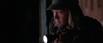 Movie still from “At Close Range” (1986), directed by James Foley – A man holding a flashlight in front of a window; Close Up shot, Over the shoulder angle