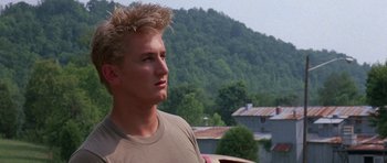 Movie still from “At Close Range” (1986), directed by James Foley – A young man is standing in front of some trees; Close Up shot, Low angle