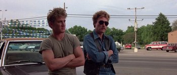 Movie still from “At Close Range” (1986), directed by James Foley – A couple of men standing next to each other on a street; Medium shot, Low angle