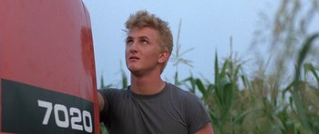 Movie still from “At Close Range” (1986), directed by James Foley – A young man holding onto a pole in a field; Close Up shot, Low angle