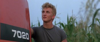 A young man holding onto a pole in a corn field